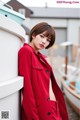 A woman in a red coat leaning against a wall.