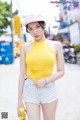 A woman in a yellow tank top and denim shorts posing for a picture.