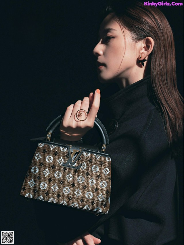 A woman in a black coat holding a brown and white handbag.