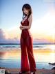 A woman in a red jumpsuit standing on a beach.